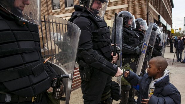 A young boy greets police officers in riot gear during a march in Baltimore after the decision to charge six officers, including one with murder.