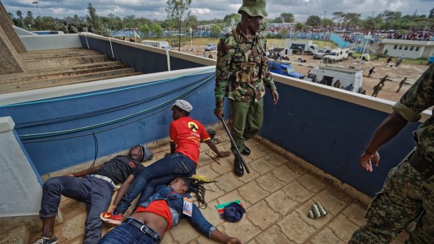 A policeman stands next to supporters of Kenyan President Uhuru Kenyatta lying unconscious after being beaten by police when they tried to storm his inauguration.