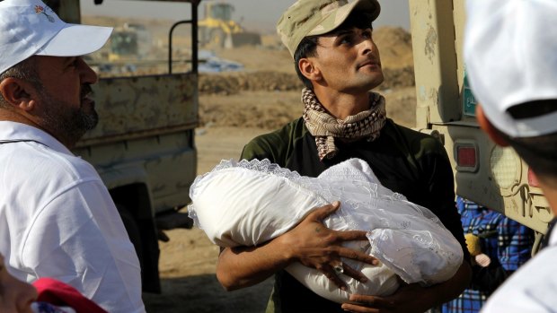 An Iraqi soldier cradles an infant after their family's arrival at a camp in Khazer, Iraq, on Tuesday.