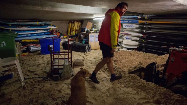 Andrew Tooher with dog Lana inspecting sand that filled the surf lifesavers' boat shed.