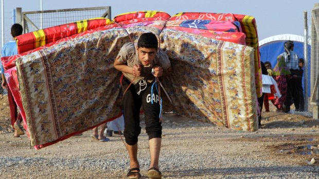 An Iraqi youth from Mosul carries mattresses at a camp in Khazer, Iraq, on Tuesday.