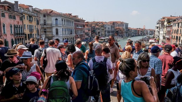 A large crowd  of tourists stand on Rialto bridge in Venice, Italy. 