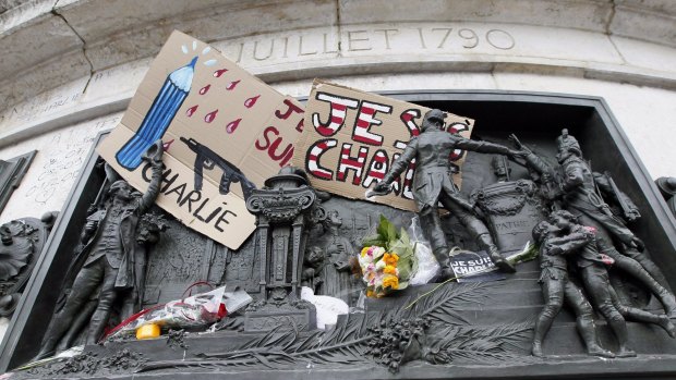 A placard with a news cartoon by French cartoonist Plantu is seen placed amongst other tributes on the statues at the Place de la Republique in Paris.
