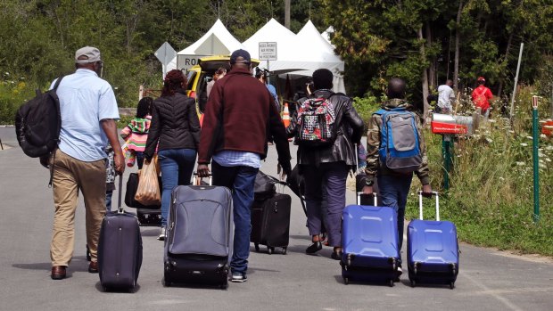 A family from Haiti approach a tent in Saint-Bernard-de-Lacolle, Quebec, stationed by Royal Canadian Mounted Police, as they haul their luggage down Roxham Road in Champlain, NY. 