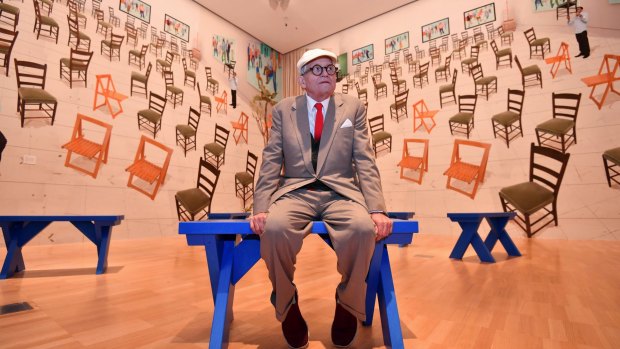Hockney with his work <i>4 blue stools</i>, 2014, featuring wallpaper comprised of stitched-together digital images.