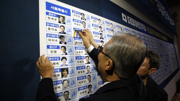 Kim Chong In, chairman of the opposition Minjoo Party of Korea, places a sticker onto one of the party's winning candidates' photographs in Seoul on Wednesday.