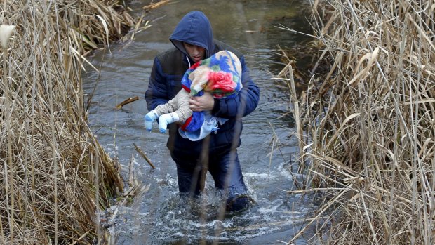A Kosovar man wades through the water while carrying his child as they illegally cross the Hungarian-Serbian border in February.