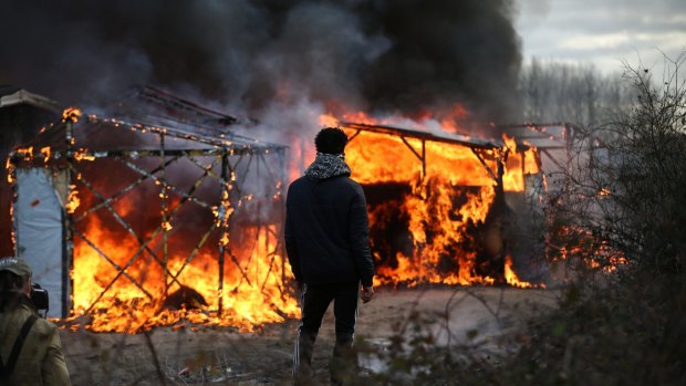A migrant watches a hut burn as police officers clear part of the Jungle migrant camp on Monday.