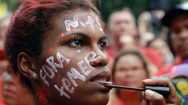 A demonstrator with the Portuguese words "Temer out" holds has her make-up applied during a protest demanding the impeachment of Brazil's President Michel Temer in Sao Paulo.
