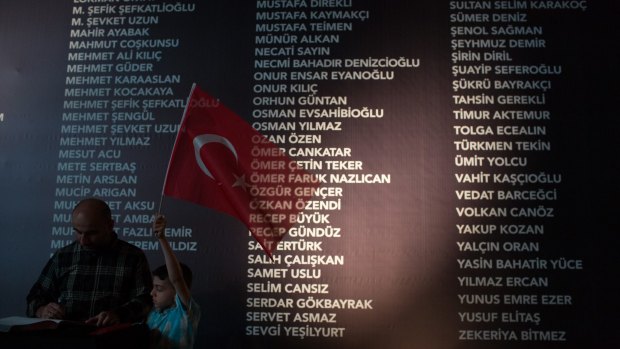 A young boy holds a Turkish flag in front of a board, at Taksim Square, listing the names of people killed during last week's failed coup attempt. The death toll now stands at 246 and 1536 wounded. 