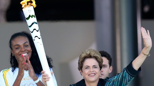 Dilma Rousseff, President of Brazil, hands the Olympic torch to the first torch bearer, Brazilian volleyball player Fabiana Claudino.