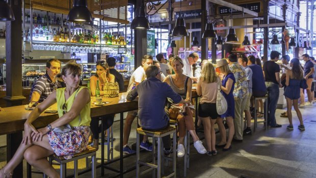 Crowds of tourists and locals enjoying drinks and tapas under the cast iron vault of the Mercado de San Miguel, the iconic market in the heart of Madrid. 