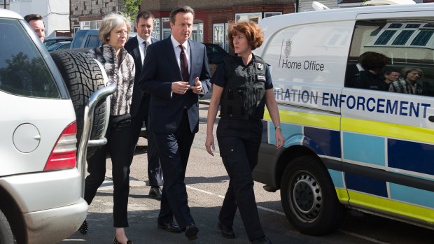 British Prime Minister David Cameron and Home secretary Theresa May (left) are accompanied by immigration enforcement officers into a home in Southall in London following an early morning raid.