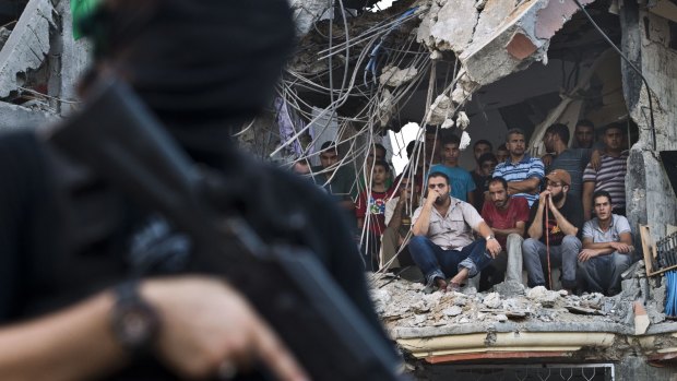 Palestinians sit in the rubble of a building as they watch Hamas militants parade their weapons in Shujaiya on Wednesday.
