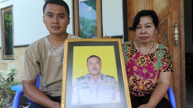 The widow of Wayan Sudarsa, Ketut Arsini, and her son Kadek Toni, hold a portrait of the police officer.