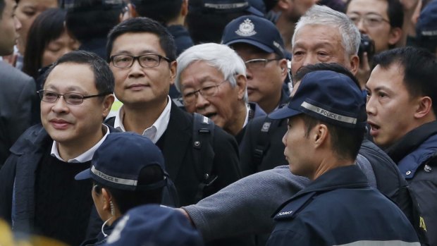 Four protest leaders, from left, Benny Tai Yiu-ting, Chan Kin-man, Joseph Zen and Chu Yiu-ming, surrounded by police officers, walk to the police station in Hong Kong as they surrender.