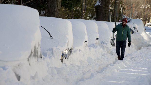 Ben Osborn walks with a shovel past a line of snowed-in cars A Steet in northeast Washington on Sunday.