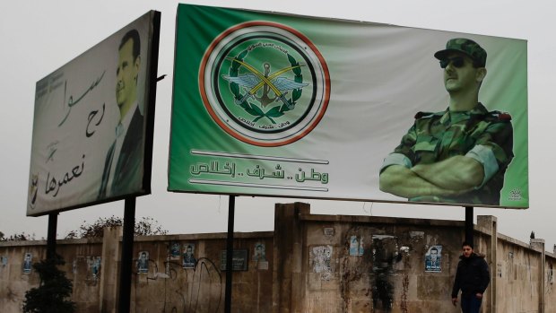 A man walks by posters of Syrian President Bashar Assad with Arabic that reads "Homeland, honour, fidelity. Together we will build it," in Aleppo. 