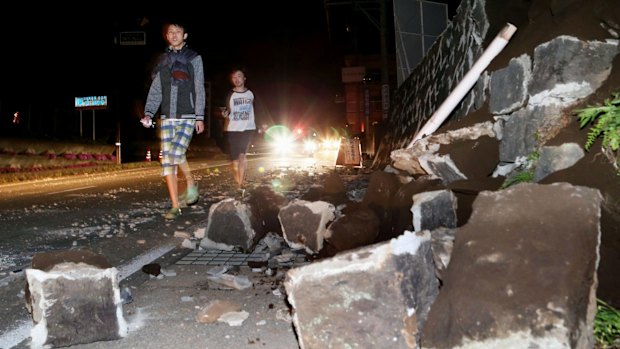 People walk past fallen walls in Mashiki.