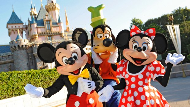Mickey Mouse, Goofy and Minnie Mouse welcome visitors in front of Sleeping Beauty Castle at Disneyland.