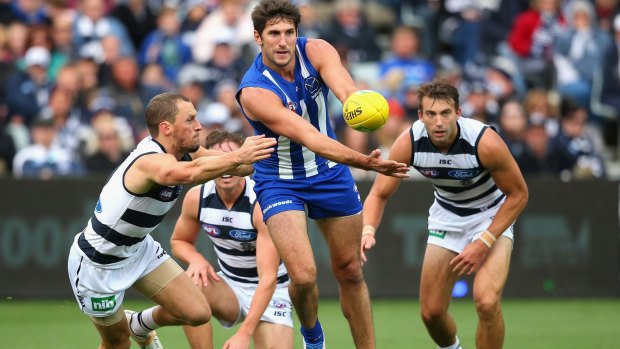 Jarrad Waite of the Kangaroos handballs as he is tackled by James Kelly of the Cats.