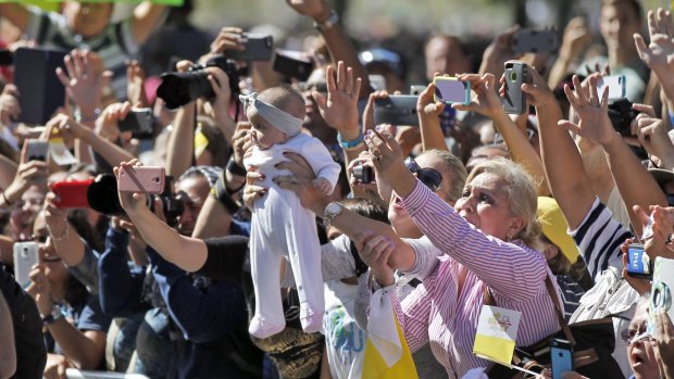 A baby is held up and a crowd reacts as Pope Francis goes by in the popemobile during a parade in Washington.