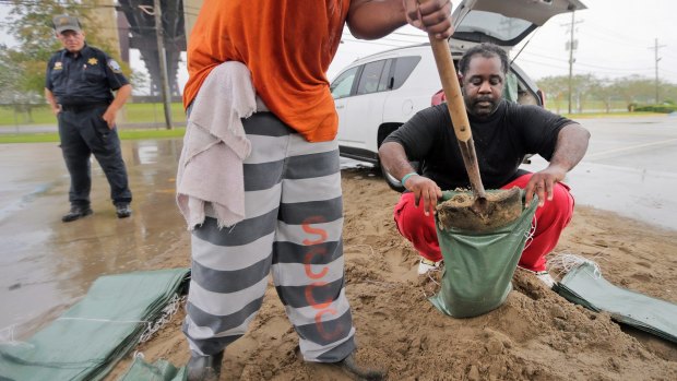 Louisiana resident Jarmar Gross, right, holds a bag as a prison trustee fills it with sand in preparation for Hurricane Nate.