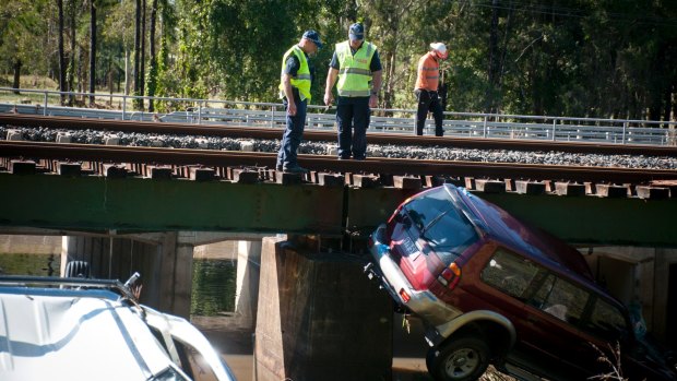 Police recover vehicles swept off a bridge by floodwaters.