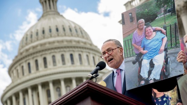 Democratic Senator Chuck Schumer holds up a photograph of constituents who would be adversely affected by the healthcare bill at a rally on Tuesday.