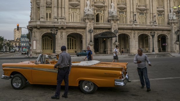 A driver hurries back to his car as a police officer stands next to it, in front of the Gran Teatro de La Habana Alicia Alonso, where President Barack Obama is scheduled to speak.