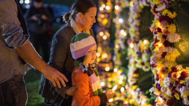 A young girl is guided to place a candle on a flower wall.