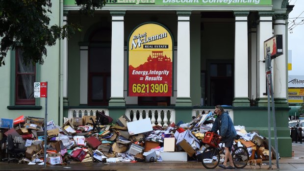 A man and his dog walk past piles of water-damaged items.