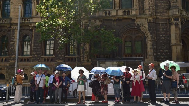 Tourists shield themselves from the hot weather under umbrellas as they wait for a tram on LaTrobe Street in the CBD on March 8.