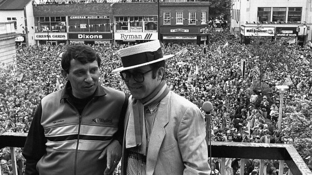Watford Football Club Chairman and pop singer Elton John, right, stands with team manager Graham Taylor on a balcony overlooking a crowd of well wishers in 1984. 