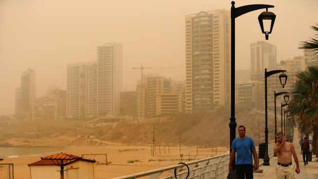 Lebanese walk on the Ramlet al-Baida seaside as a sandstorm shrouds the coastal capital of Beirut.