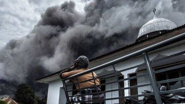 An Indonesian woman looks on as Mount Sinabung spews ash.