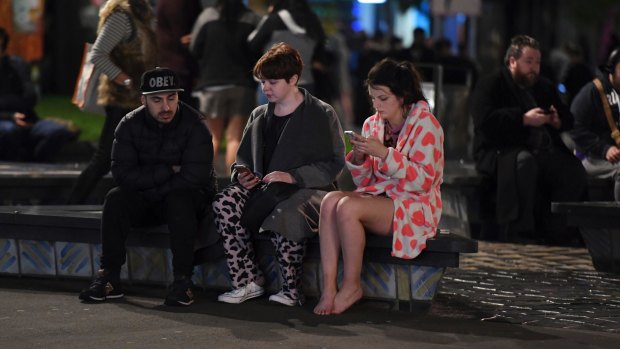 People evacuated from buildings in Wellington check their mobile phones.