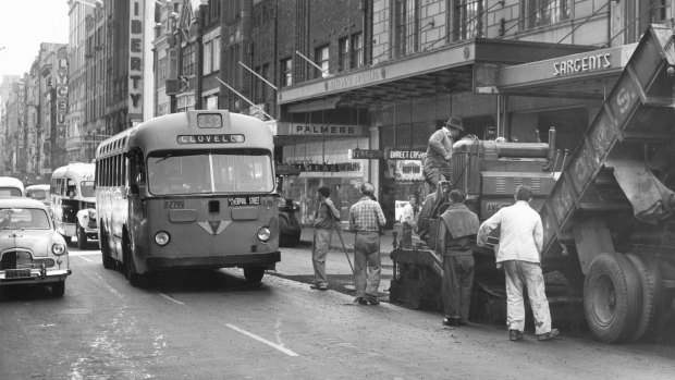 A 339 Clovelly bus swings out to pass workmen laying bitumen over tramlines on Pitt Street on October 1, 1957. 