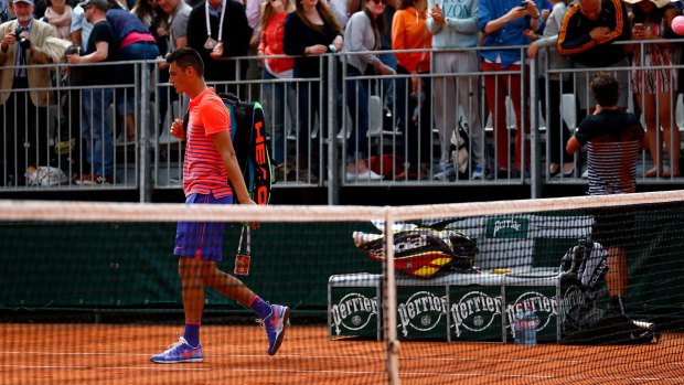 Australia's Bernard Tomic leaves the court as compatriot Thanasi Kokkinakis speaks with fans after their match at the French Open.