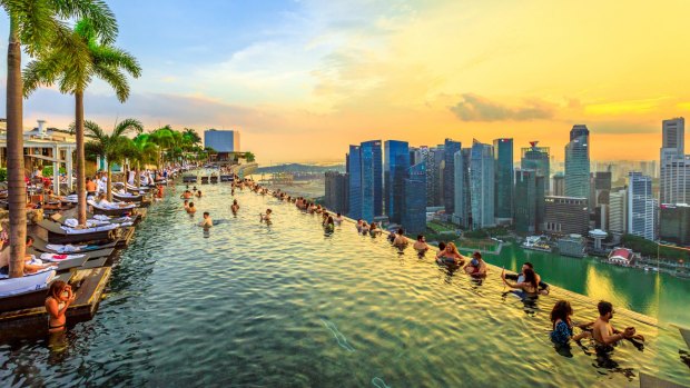 Singapore - May 3, 2018: Infinity Pool at sunset of Skypark that tops the Marina Bay Sands Hotel and Casino from rooftop of La Vie Club Lounge on 57th floor. Financial district skyline on background. singapore