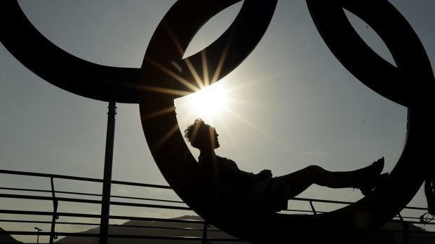 A woman is silhouetted by the setting sun in a set of Olympic rings in the Olympic Park ahead.