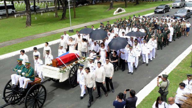 Imelda Marcos, in black on a wheelchair under an umbrella, widow of the late dictator Ferdinand Marcos, and their close relatives follow his flag-draped coffin to his burial at the Heroes' Cemetery on Friday.