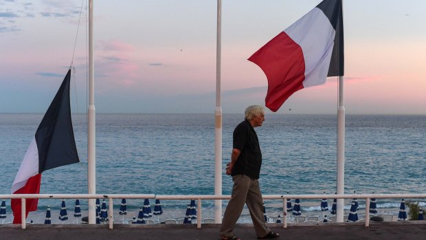 A man walks past French flags flying at half-mast on the Promenade des Anglais in Nice, France, the day after a French-Tunisian attacker killed 84 people as he drove a lorry through Bastille Day crowds.