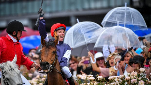 Jockey Kerrin McEvoy celebrates after winning the Melbourne Cup, as racegoers brought out their umbrellas. 