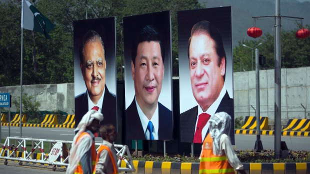 Workers walk past a billboard showing pictures of Chinese President Xi Jinping, centre, with Pakistani President Mamnoon Hussain, left, and Prime Minister Nawaz Sharif in Islamabad, Pakistan.