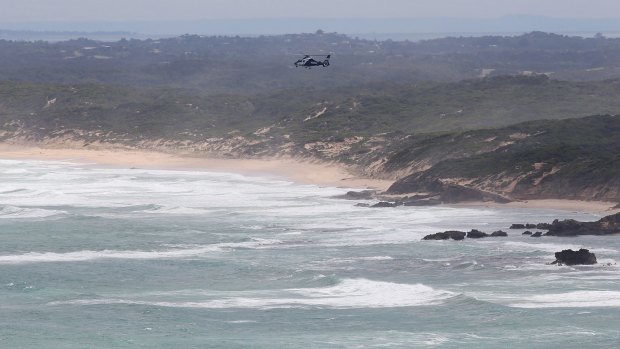 A search and rescue helicopter hovers over where two fishermen are missing in waters off Cape Schanck, on the Mornington Peninsula.