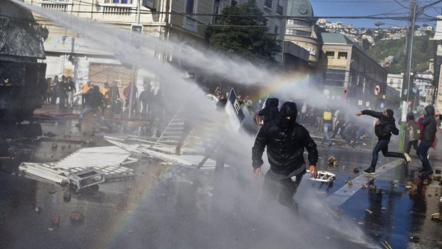 Masked protesters throw stones at a water cannon near where President Michelle Bachelet was presenting the state-of-the-nation report on Saturday.