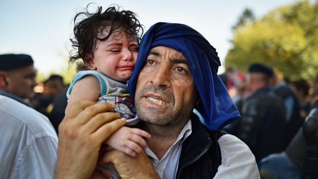A man holds his crying child close to him as migrants force their way through police lines at Tovarnik station for a train to take them to Zagreb, Croatia on Thursday.