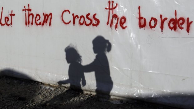 Shadows of children are cast on a tent bearing graffiti at the northern Greek border point of Idomeni, Greece, on Wednesday.