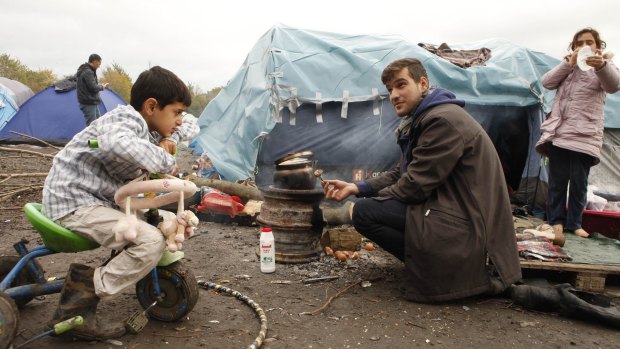 A migrant from Iraq prepares roasted mushrooms as children watch in a makeshift camp in Dunkirk, northern France.